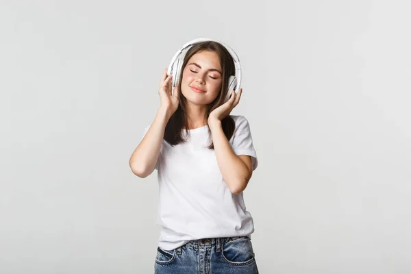 Sonhador menina bonita gostando de ouvir música em fones de ouvido sem fio, sorrindo feliz — Fotografia de Stock