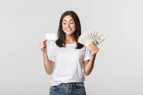 Портрет взволнованной улыбающейся девушки с деньгами и кредиткой на белом фоне — стоковое фото