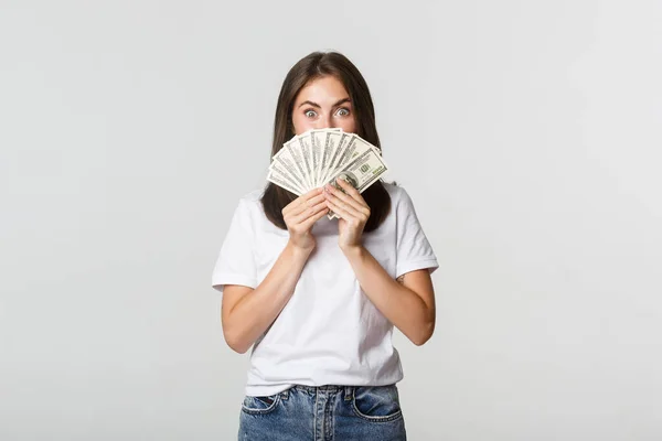 Emocionado bastante joven mujer sosteniendo el dinero sobre la cara, de pie fondo blanco — Foto de Stock