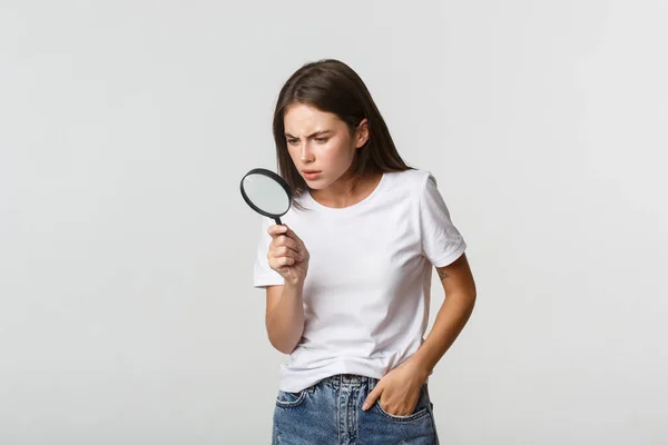 Sério-olhando menina bonita inteligente olhando através de lupa para baixo, à procura de algo — Fotografia de Stock