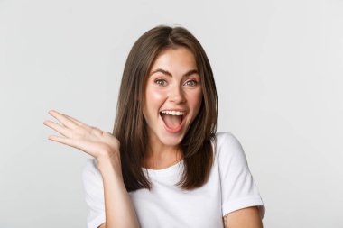 Heyecanlı, güzel esmer kızın yakın plan fotoğrafı. Eğlenmiş görünüyor. El sallayarak merhaba diyor.