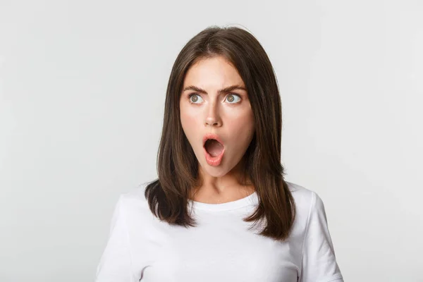 Portrait of impressed pretty girl looking left, drop jaw and gasping astonished, white background — Stock Photo, Image