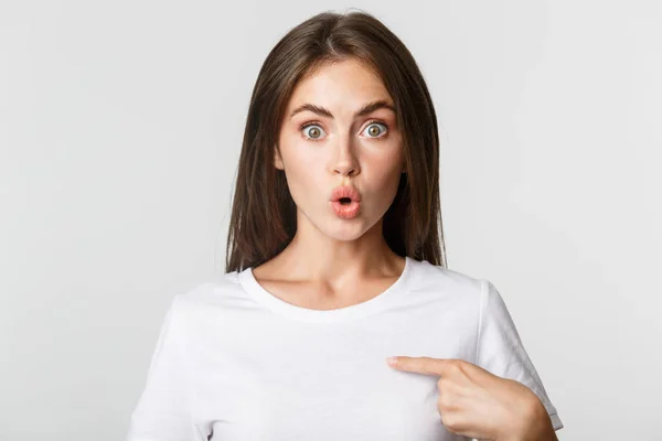 Detailní záběr překvapené a vzrušené mladé brunetky dívka ukazuje na sebe, bílé pozadí — Stock fotografie