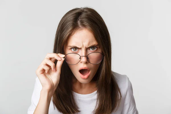 Primer plano de la mujer enojada joven insultada y conmocionada mirando desde debajo de las gafas — Foto de Stock