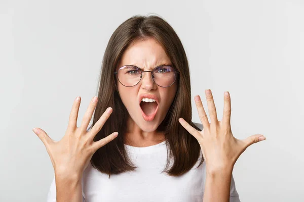 Close-up of angry and furious young woman in glasses arguing, complaining over white background — Stock Photo, Image