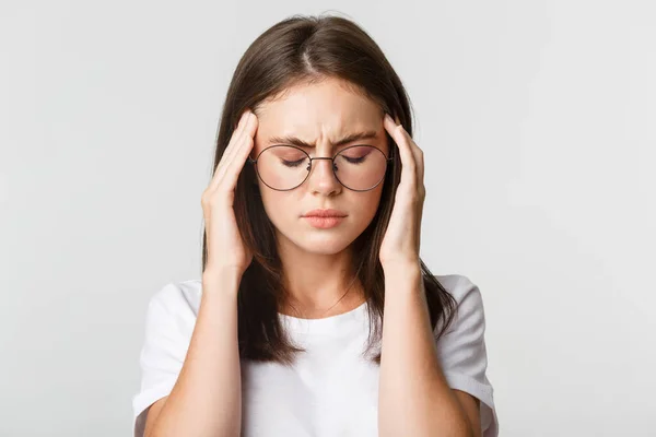 Primo piano di giovane donna in occhiali che tocca la testa e smorfia dal dolore, ha mal di testa o emicrania, si sente male — Foto Stock