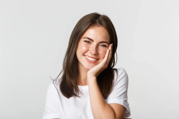 Primer plano de hermosa chica morena sonriente tocando mejillas, ruborizándose sobre fondo blanco —  Fotos de Stock