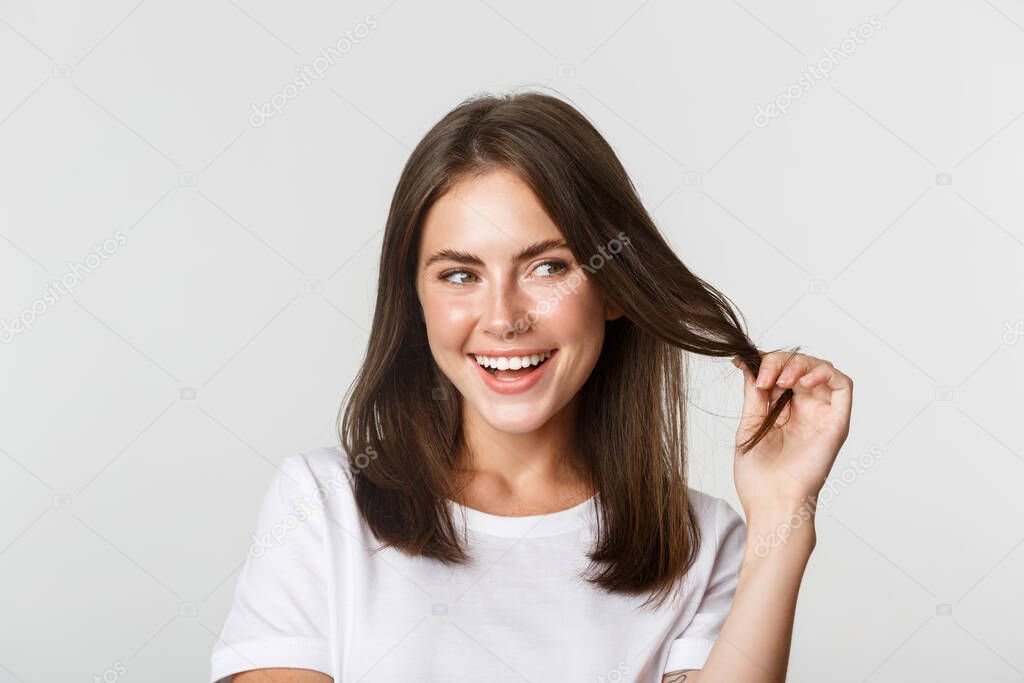 Close-up of flirty attractive brunette girl playing with hair strand, smiling and looking intrigued to the right