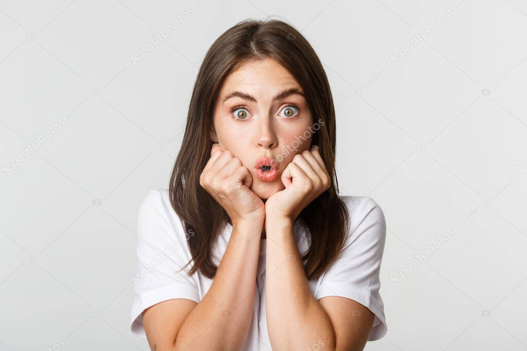 Close-up of intrigued young gossiping girl, leaning on hands and looking wondered at camera, gasping impressed, white background