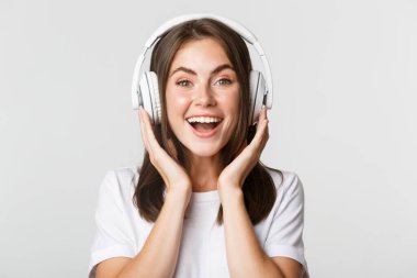 Gülümseyen, kulaklıkla müzik dinleyen, ilginç podcastlardan hoşlanan esmer kızın yakın çekimi.