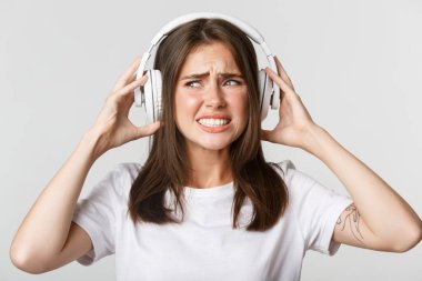 Kablosuz kulaklıklar takmış, rahatsız edici müzik ve somurtkanlıktan şikayetçi güzel bir kızın yakın çekimi.