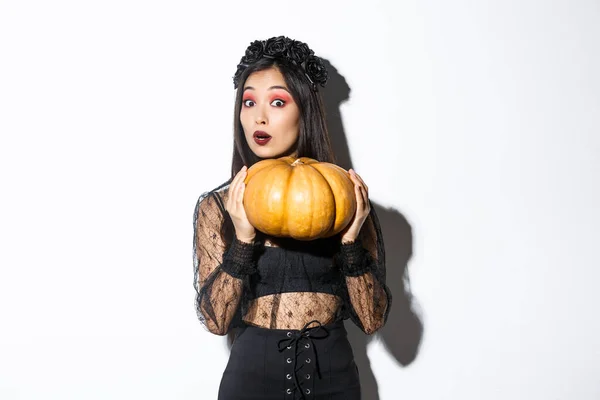 Portret van een vrouw die zware pompoen optilt, zich klaarmaakt voor Halloween, heksenkostuum draagt, over een witte achtergrond staat — Stockfoto