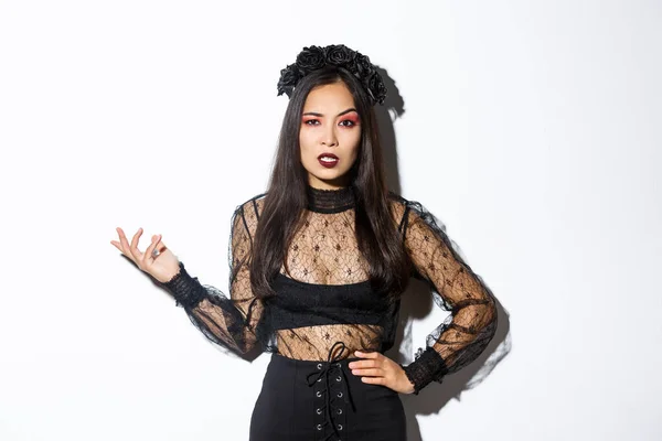 Angry and confused asian woman in witch costume looking bothered by annoying quetion, raising hand up and stare at camera pissed-off. Female at halloween party standing frustrated — Stok fotoğraf