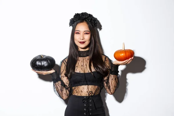Blij lachende aziatische vrouw vieren Halloween, het dragen van heks kostuum, het vasthouden van pompoenen, staande over witte achtergrond — Stockfoto