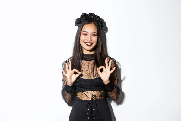 Alegre hermosa mujer asiática en vestido de bruja mostrando gestos bien y sonriendo satisfecho, aprobar disfraz de halloween o anuncio, de pie sobre fondo blanco —  Fotos de Stock