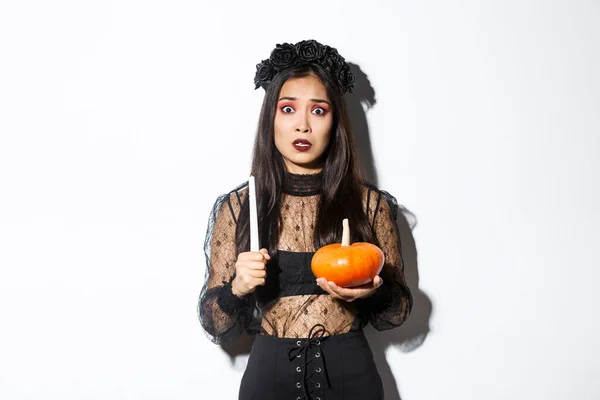 Afbeelding van Aziatische vrouw in paniek, bang van hekserij op Halloween, staande in heks kostuum met kaars en pompoen — Stockfoto