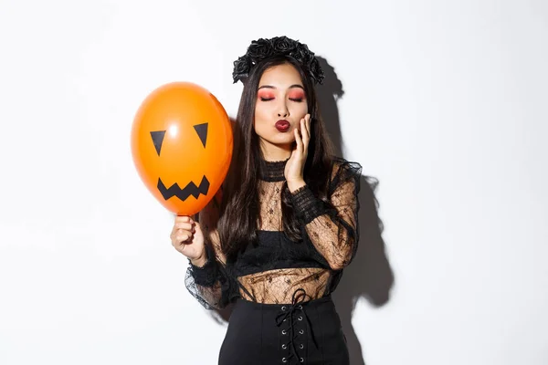 Afbeelding van mooie stijlvolle aziatische vrouw vieren halloween, het dragen van heks kostuum, met oranje ballon met gezicht — Stockfoto