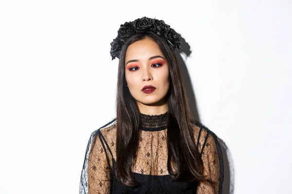 Primer plano de aburrido y molesto asiático mujer en halloween traje de bruja entrecerrar los ojos, tratando de mirar a la nariz, de pie sobre fondo blanco —  Fotos de Stock