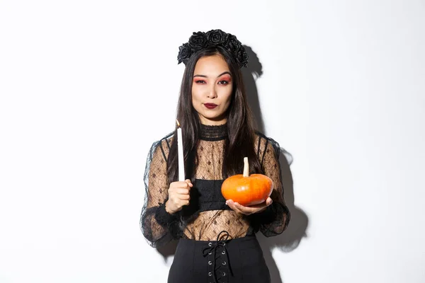 Imagen de hermosa mujer asiática en traje de bruja, sosteniendo vela encendida y calabaza, celebrando halloween —  Fotos de Stock