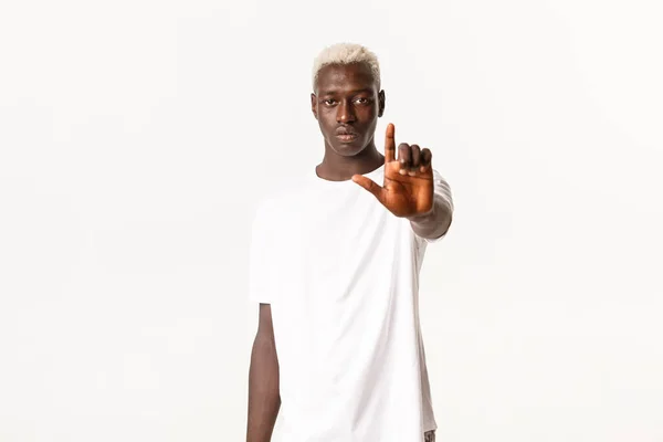 Retrato de un joven guapo afroamericano serio, extender la mano y mostrar el dedo, detener o desaprobar algo, oferta de aversión, regañar a la persona, fondo blanco — Foto de Stock