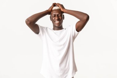 Karmaşık, endişeli, Afro-Amerikan sarışın bir adamın portresi, el ele tutuşmuş, paniğe kapılmış, beyaz arka planda duruyor.
