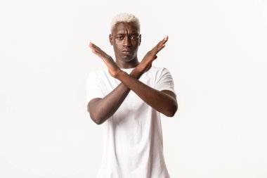 Ciddi Afro-Amerikan sarışın bir adamın portresi, kötü bir şeyi durdurmak için çapraz jest yapıyor, onaylamıyor, yasaklıyor, beyaz arka planda duruyor.