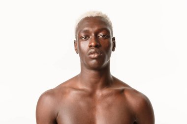 Ciddi görünüşlü, Afro-Amerikan yakışıklı, sarı saçlı, göğsü beyaz arka planda, kararlı görünüyor.