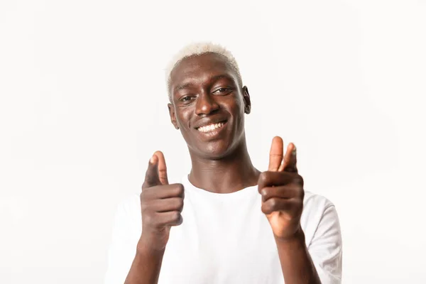 Primer plano de apoyo guapo afroamericano rubio chico apuntando con los dedos a la cámara y sonriendo, felicitando, alabando buena elección, de pie sobre fondo blanco — Foto de Stock