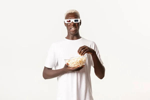 Porträt eines angeekelten afrikanisch-amerikanischen Blonden, der sich etwas Unangenehmes ansieht, aus dem Film kratzt, 3D-Brille trägt und Popcorn isst, weißer Hintergrund — Stockfoto