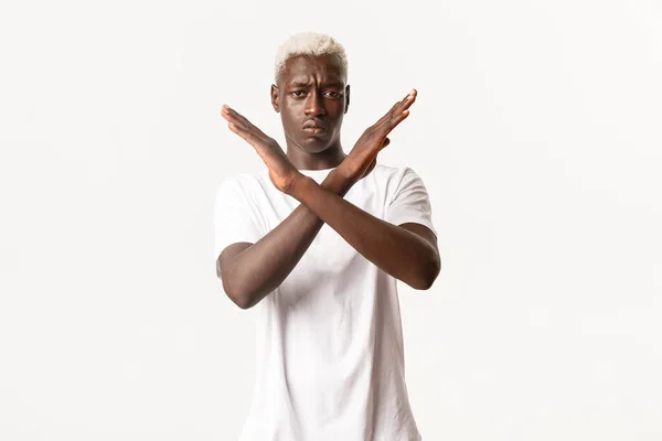Портрет серьезного африканско-американского блондина, делающего перекрестный жест, чтобы остановить что-то плохое, не одобряющего действия, запрещающего, стоящего на белом фоне — стоковое фото
