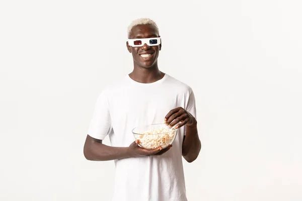 Retrato de chico rubio afroamericano atractivo feliz comiendo palomitas de maíz y viendo películas en gafas 3d, sonriente alegre, de pie fondo blanco — Foto de Stock