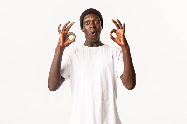 Portrait of surprised and impressed african-american male customer, showing okay gestures and looking excited, recommend product, standing white background.