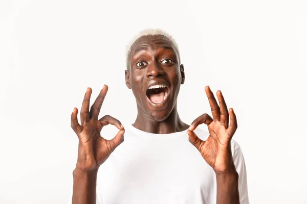 Close-up van opgewonden aantrekkelijke Afrikaans-Amerikaanse blonde man uiten verbazing, tonen oke gebaar in goedkeuring, staande witte achtergrond — Stockfoto