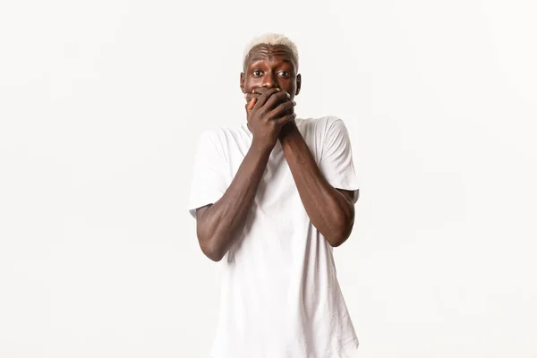 Retrato de chico rubio afroamericano sorprendido y sorprendido, jadeando con la boca cubierta, mirando sobresaltado, de pie fondo blanco — Foto de Stock