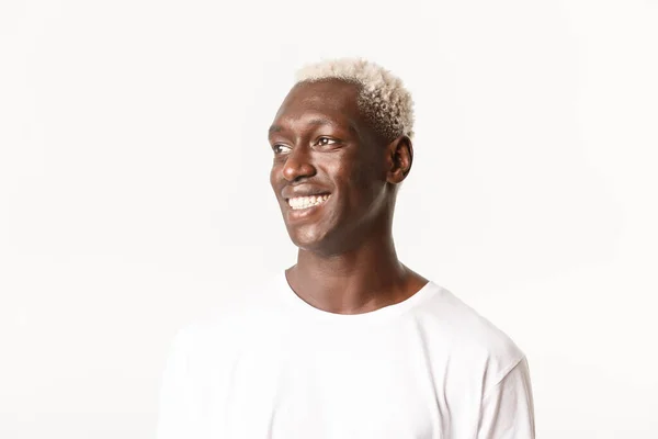 Zbliżenie pełnego nadziei i szczęśliwego, przystojnego afrykańsko-amerykańskiego młodzieńca odwracającego wzrok z uśmiechem na twarzy, stojącego na białym tle — Zdjęcie stockowe