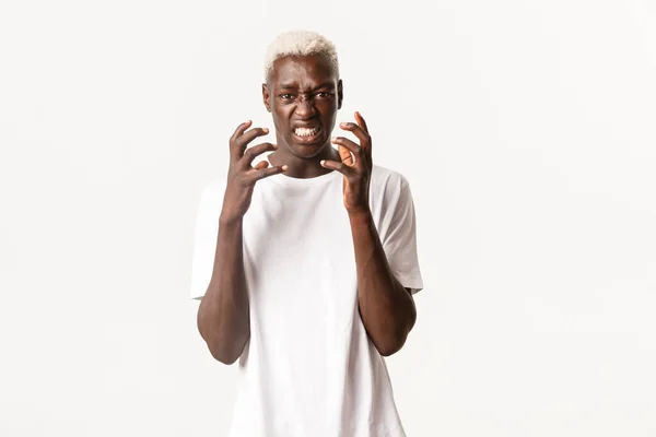 Portret van een boze Afrikaans-Amerikaanse blonde man, handen klemmen en er hatelijk uitzien, zich verontwaardigd of gestoord voelen, over een witte achtergrond staan — Stockfoto