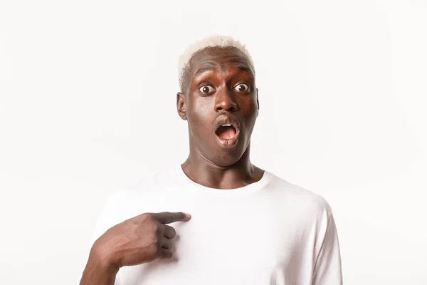 Retrato de un rubio afroamericano sobresaltado que parece sorprendido al apuntarse a sí mismo con la mandíbula caída, de pie sobre fondo blanco — Foto de Stock