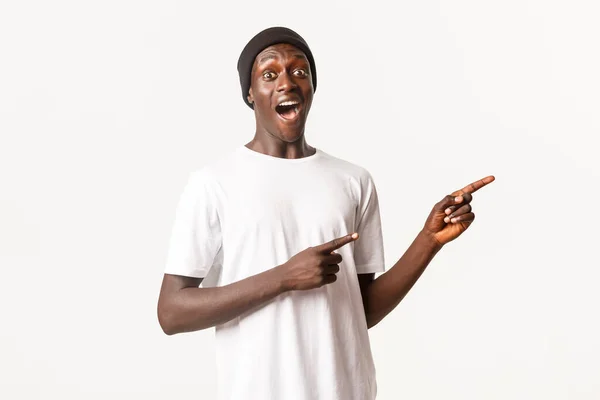 Retrato de divertido cara afro-americano bonito, boca aberta maravilhado e apontando os dedos direito, de pé fundo branco — Fotografia de Stock