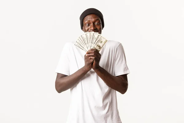 Retrato de chico afortunado afro-americano emocionado y complacido, sosteniendo el dinero del premio y mirando en efectivo tentado, fondo blanco —  Fotos de Stock
