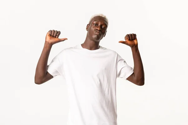 Porträtt av självsäker vacker afrikansk-amerikansk blond kille, pekar fingrarna på sig själv kaxig och stolt, står över vit bakgrund — Stockfoto