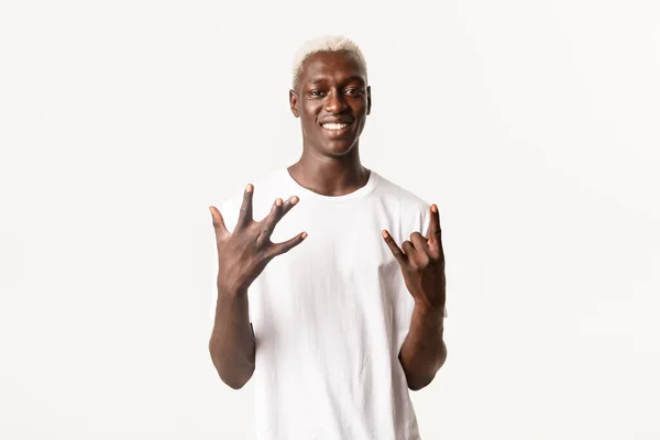 Portret van een stijlvolle Afrikaans-Amerikaanse blonde man met West Coast handteken en rock-on, lachende vrolijke, staande witte achtergrond — Stockfoto