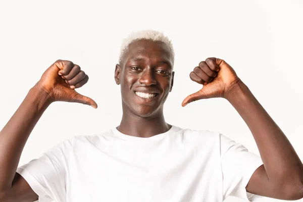 Primer plano de seguro guapo afroamericano rubio chico apuntando a sí mismo orgulloso y asertivo, sonriendo sobre fondo blanco — Foto de Stock