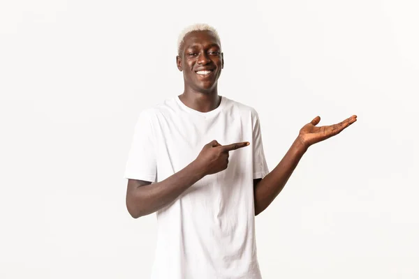 Πορτρέτο του χαμογελαστού περήφανου Αφροαμερικανού που δείχνει το χέρι, κρατάει κάτι, στέκεται λευκό φόντο — Φωτογραφία Αρχείου