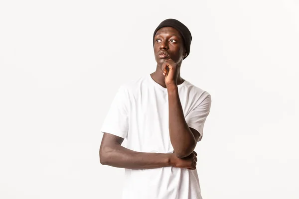 Retrato de hombre afro-americano con estilo reflexivo en gorro, mirando a la izquierda y reflexionando, haciendo elección, de pie fondo blanco — Foto de Stock