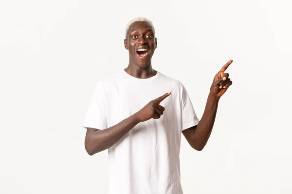 Retrato de cara afro-americano surpreso e animado, olhando dedos fascinados e apontando canto superior direito, fundo branco — Fotografia de Stock