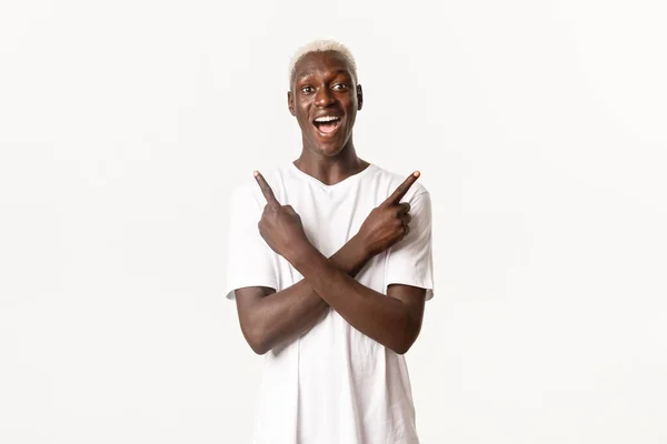 Portré boldog és izgatott, vonzó afro-amerikai szőke férfi, ujjal oldalra mutató és mosolygós csodálkozó, fehér háttér — Stock Fotó