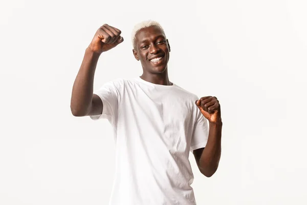 Retrato de alegre loiro afro-americano, ganhando e sorrindo feliz, regozijando-se com a vitória, de pé fundo branco e triunfando — Fotografia de Stock