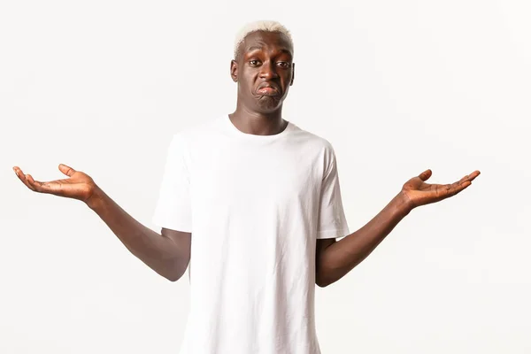 Porträt eines ahnungslosen attraktiven afrikanisch-amerikanischen blonden Mannes, die Hände zur Seite gespreizt und achselzuckend, weißer Hintergrund stehend — Stockfoto