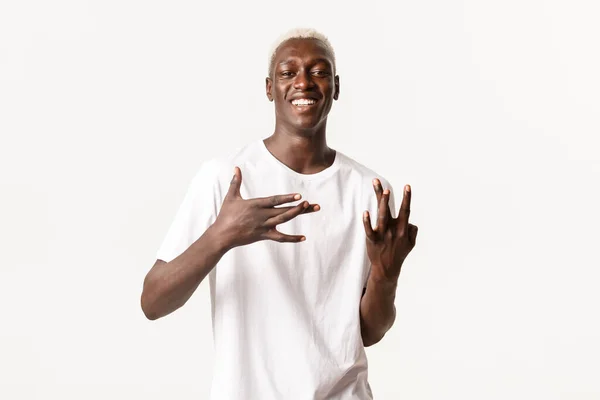 Tipo rubio afroamericano fresco y atrevido, mostrando signos de mano de la costa oeste y sonriendo ampliamente, de pie fondo blanco — Foto de Stock