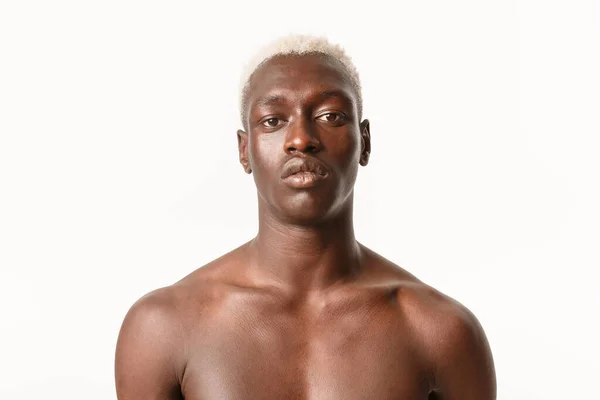 Närbild av allvarliga utseende snygg afrikansk-amerikansk kille med blont hår, står med bara bröstet över vit bakgrund, ser bestämd — Stockfoto